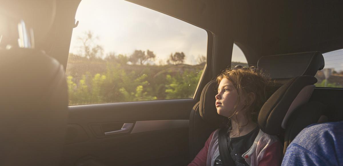 Child in car looking out through window on sunny sky