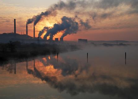 Factory pipe polluting air, beside lake