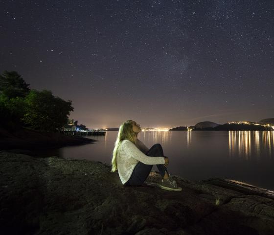 a woman sits on a cliff and looks out over a night sky
