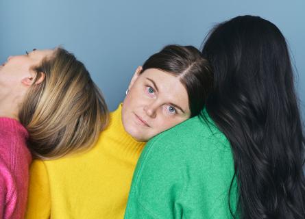 three girls standing next to each other in bright coloured sweaters